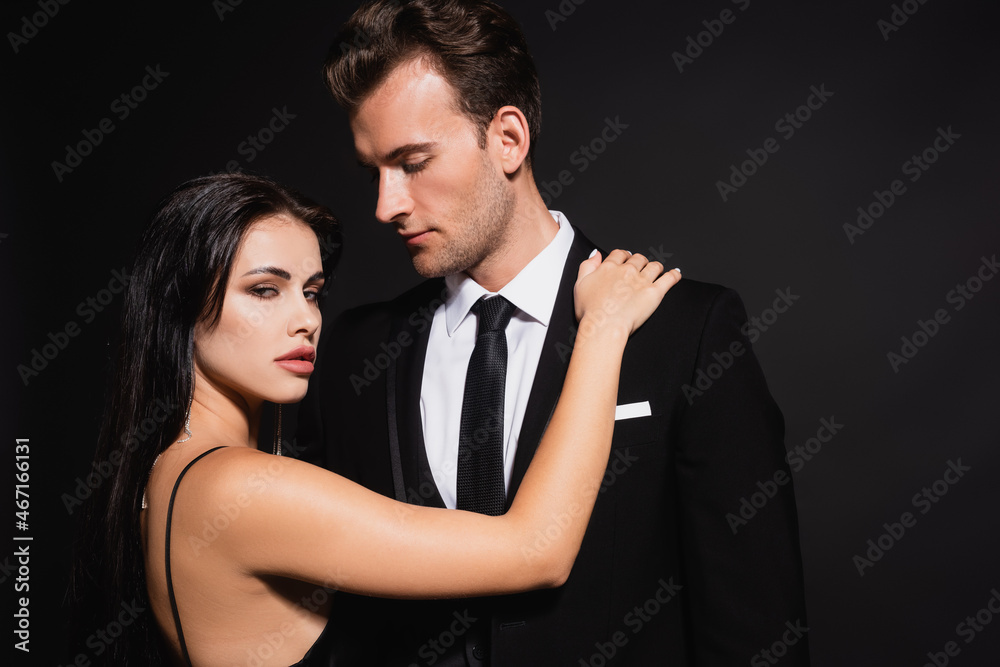 passionate woman looking at camera near man in elegant suit isolated on black passionate woman looking at camera near man in elegant suit isolated on black