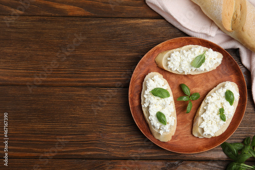 Bread with cottage cheese and basil on wooden table, flat lay. Space for text