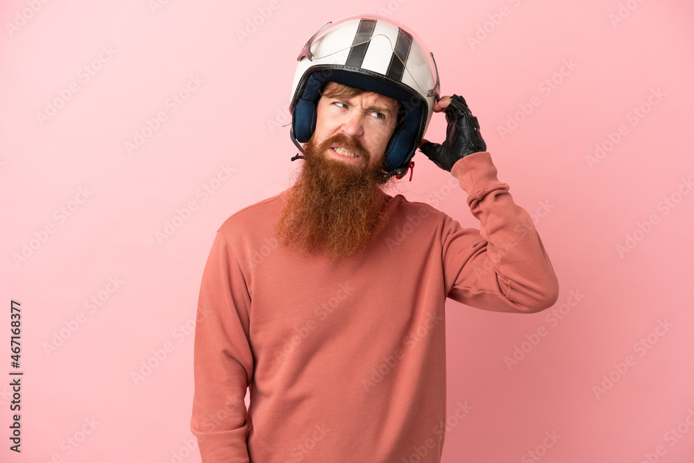 Young reddish caucasian man with a motorcycle helmet isolated on pink background having doubts Young reddish caucasian man with a motorcycle helmet isolated on pink background having doubts