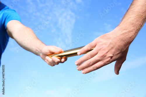 Man passing baton to his partner against blue sky, closeup