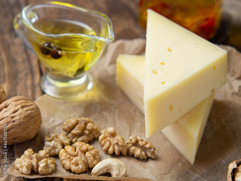 pieces of cheese on parchment paper with nuts and olive oil on an old wooden table