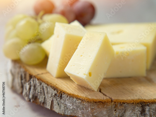 Light meal with sliced cheese next to a bunch of white and red grapes