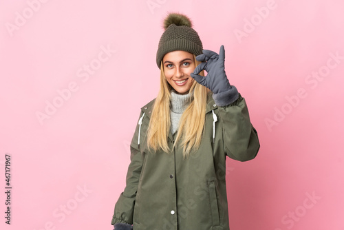 Young woman with winter hat isolated on pink background showing ok sign with fingers