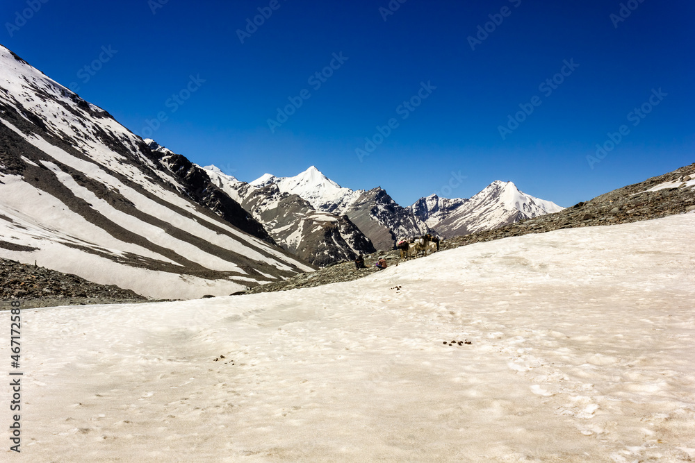 A trekking trail passing through the thick snow of the surface of a ridge with a view of snow capped Himalayan mountains of the Zanskar range near the Shingo La pass.