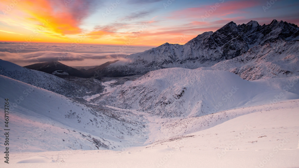 Panorama of snowy mountains in wintertime in sunrise. White hills with orange sky in winter with copy space. Ice mountainside with color skyline.