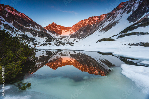 Snowy mountains in sunlit with reflection in water. White High Tatras with lake in sunlight with copy space.