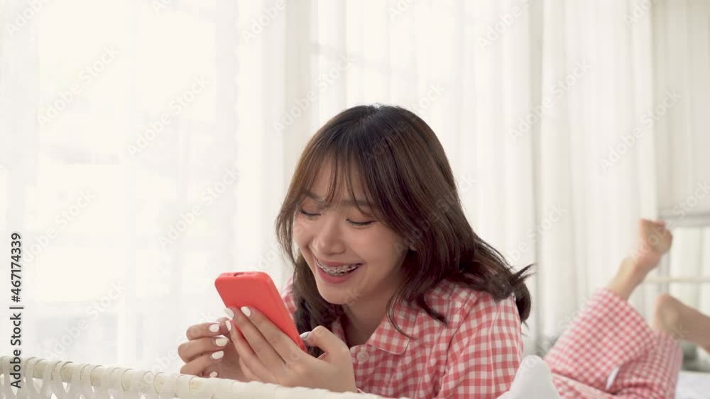 Beautiful Asian woman in red pajamas lying in bed playing mobile phone on her bed in the morning. Beautiful Asian woman in red pajamas lying in bed playing mobile phone on her bed in the morning.
