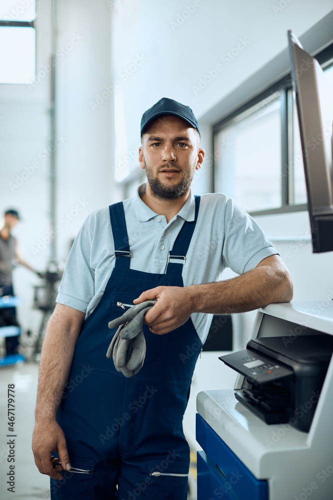 Young mechanic uses desktop PC at car workshop and looks at camera. Young mechanic uses desktop PC at car workshop and looks at camera.