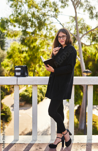 Businesswoman standing with notebook in hand near wooden railing on street