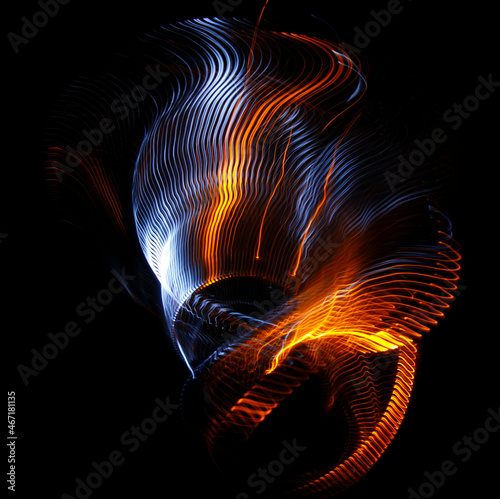 Long exposure photograph of multicolored light trails forming a complex twisted geometric pattern of parallel lines against a dark background. Only photo, no illustration.
