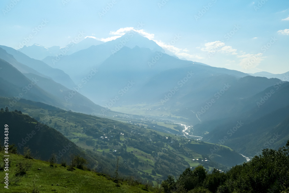 A panoramic view on Zhabeshi, a mountain village, located on the bank of the river Mulkhura in Georgia. High Caucasus mountain chains. Lush green pastures with a few cows grazing on them. Idyllic