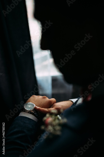 A young man in a blue suit looks at his watch. Face silhouette. The groom is waiting for the meeting with the bride.