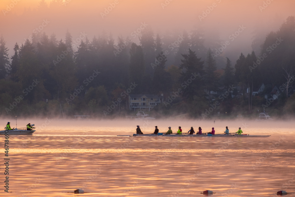 Silhouette of a crew rowing on a lake as the rising sun casts a golden glow over the water and trees in the background