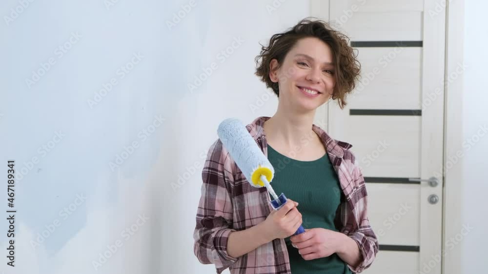A young adult cheerful woman with blue paint using a roller. Repair and renovation of the design of home room apartment. DIY repair of the house. A young adult cheerful woman with blue paint using a roller. Repair and renovation of the design of home room apartment. DIY repair of the house.