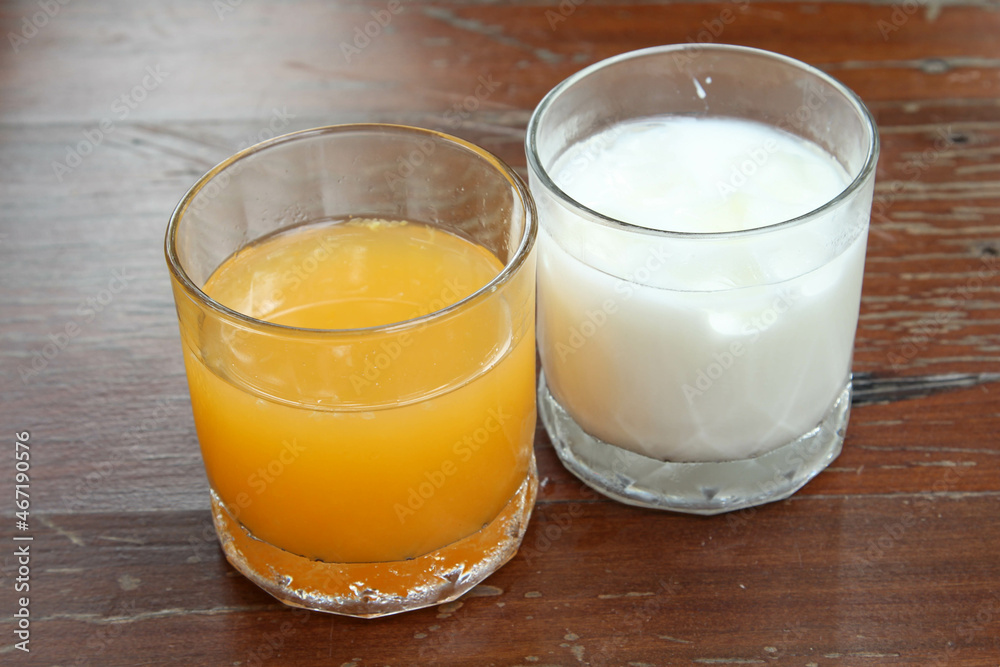 The iced milk and iced orange juice in clear glass on the wooden table. The iced milk and iced orange juice in clear glass on the wooden table.