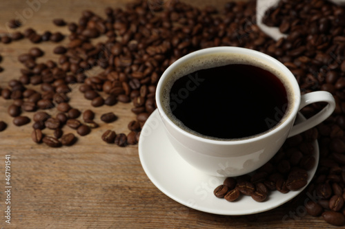 Cup of aromatic coffee and beans on wooden table, closeup. Space for text