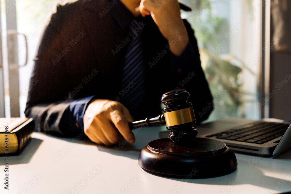 Justice and law concept.Male judge in a courtroom with the gavel, working with, computer and docking keyboard, eyeglasses, on table in morning light Justice and law concept.Male judge in a courtroom with the gavel, working with, computer and docking keyboard, eyeglasses, on table in morning light