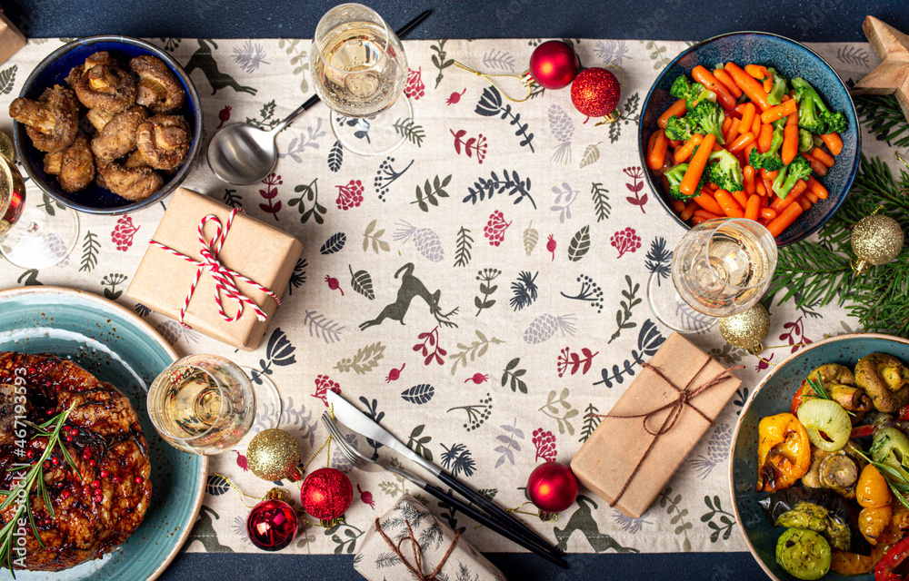 Christmas evening decorated table flat lay background with copy space with festive food, sparkling wine glasses, wrapped presents and fir tree 
