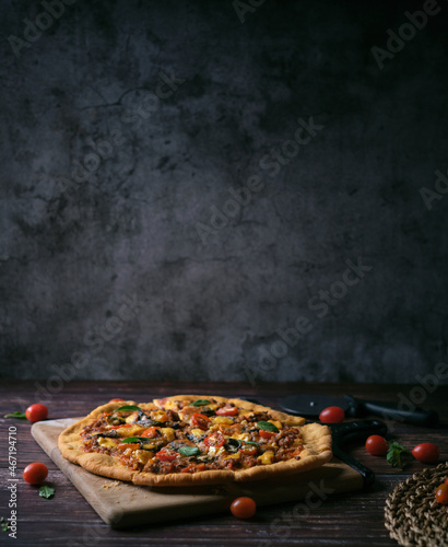 Fresh baked thin crust Italian pizza with tomato sauce pepper cheese and basil leaf on Dark rustic table background. © Tavan