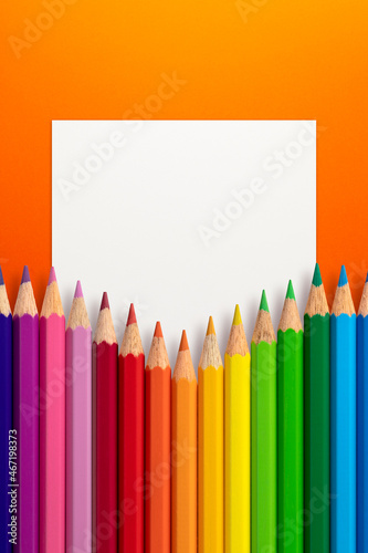 Creative layout made of color pencils on orange paper background with white paper card note. Flat lay. Education concept.