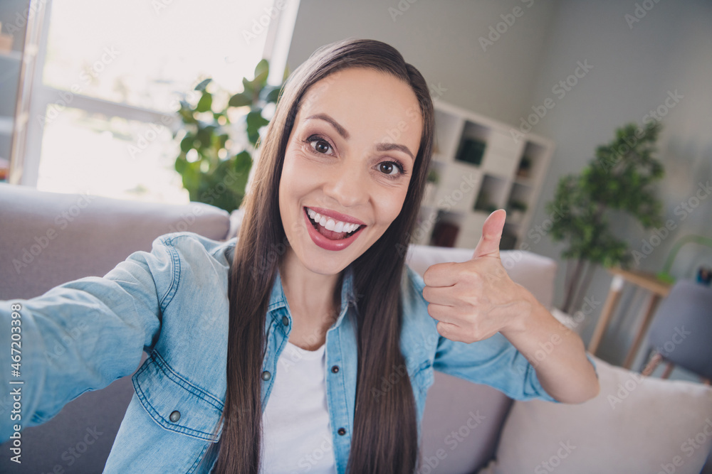 Self-portrait of attractive cheerful long-haired woman showing thumbup advert staying at home indoors