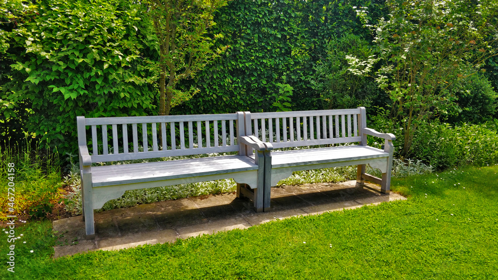 White double bench with hedgerow in the background. There is grass all over the picture and seat looks very relaxing. White double bench with hedgerow in the background. There is grass all over the picture and seat looks very relaxing.