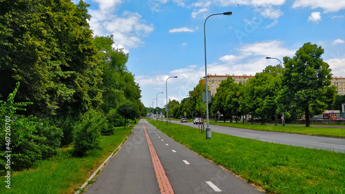 Sidewalk combined with cycleway going around the park on the left side and road on the right side. The summer weather is pleasant. There are also street lamps by the road. photo