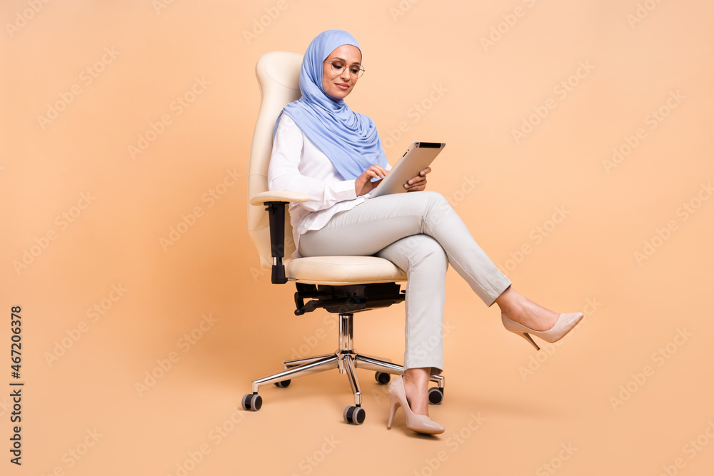 Full size photo of young arabic modern lady type tablet sit wear headscarf shirt eyewear pants stilettos isolated on beige background