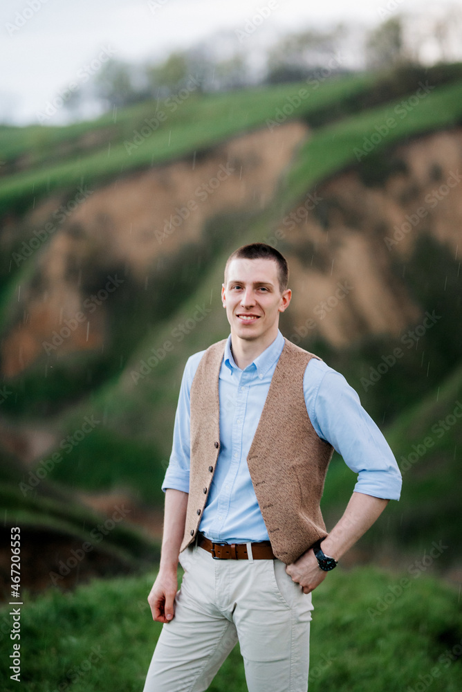 Fototapeta premium a young guy in a brown suit on the background of mountain green slopes