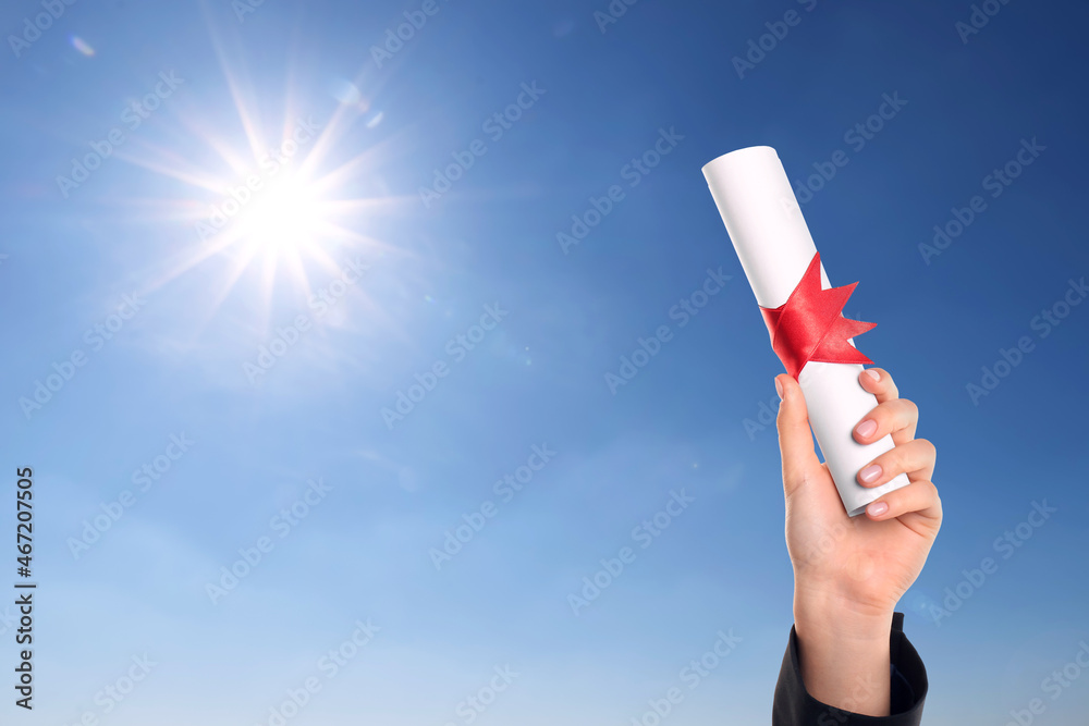 Graduated student holding diploma against blue sky on sunny day, closeup Graduated student holding diploma against blue sky on sunny day, closeup