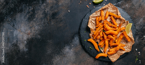 Fotografie Baked sweet potato fries on dark background