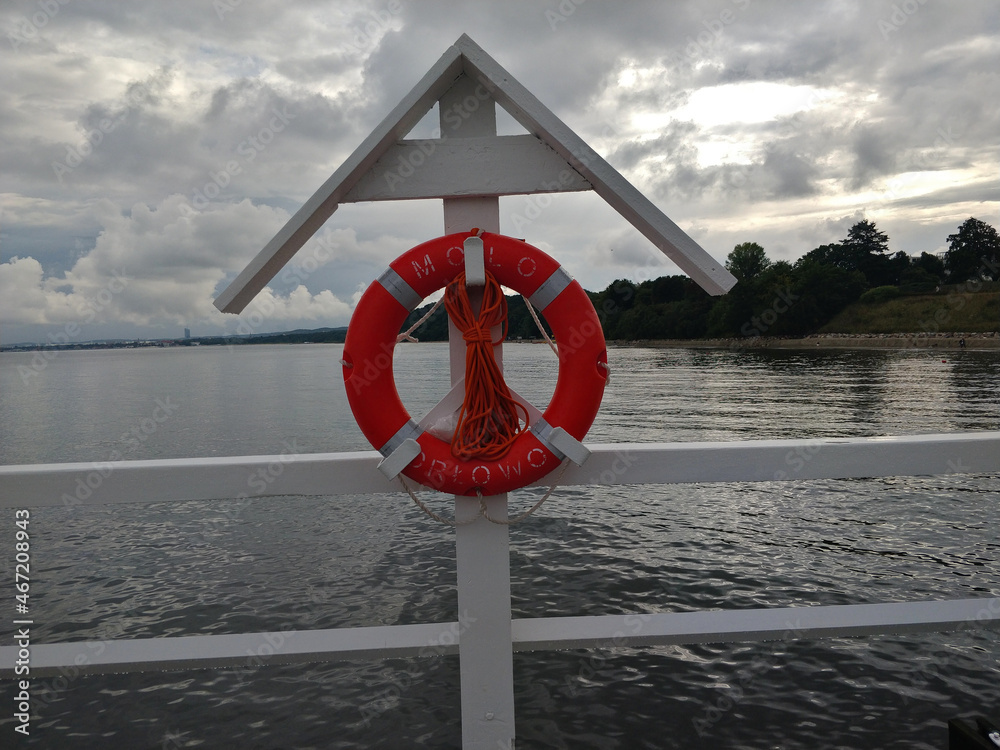 Lifebuoy prepared on the Orlowo wharf in Poland during cloudy weather. The lifebuoy is hanged on the white wooden hook.