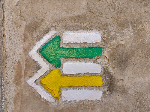 Two Czech tourist directional arrows painted on gray wall. One is green and the other is yellow. They both go in the same direction.