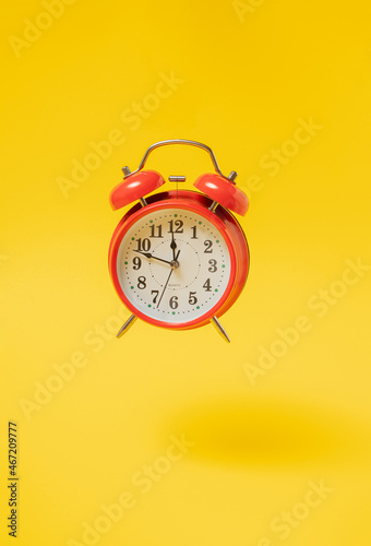 old red vintage table clock flying in the air against yellow illuminating background with shadow. Retro Christmas abstract art with copy space