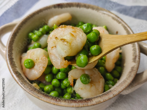 Shrimp with pea put into the beige pot with wooden spoon holding a bit of shrimp with peas. photo