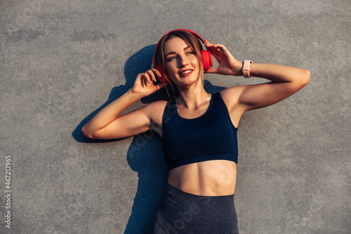 Beautiful girl with sports devices listen to music in headphones while training in front of a gray wall