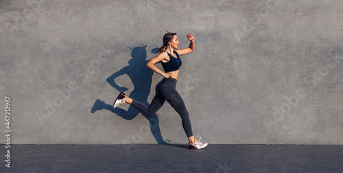 Young sportive woman jumping and running on gray background, female model in sportswear exercising outdoors
