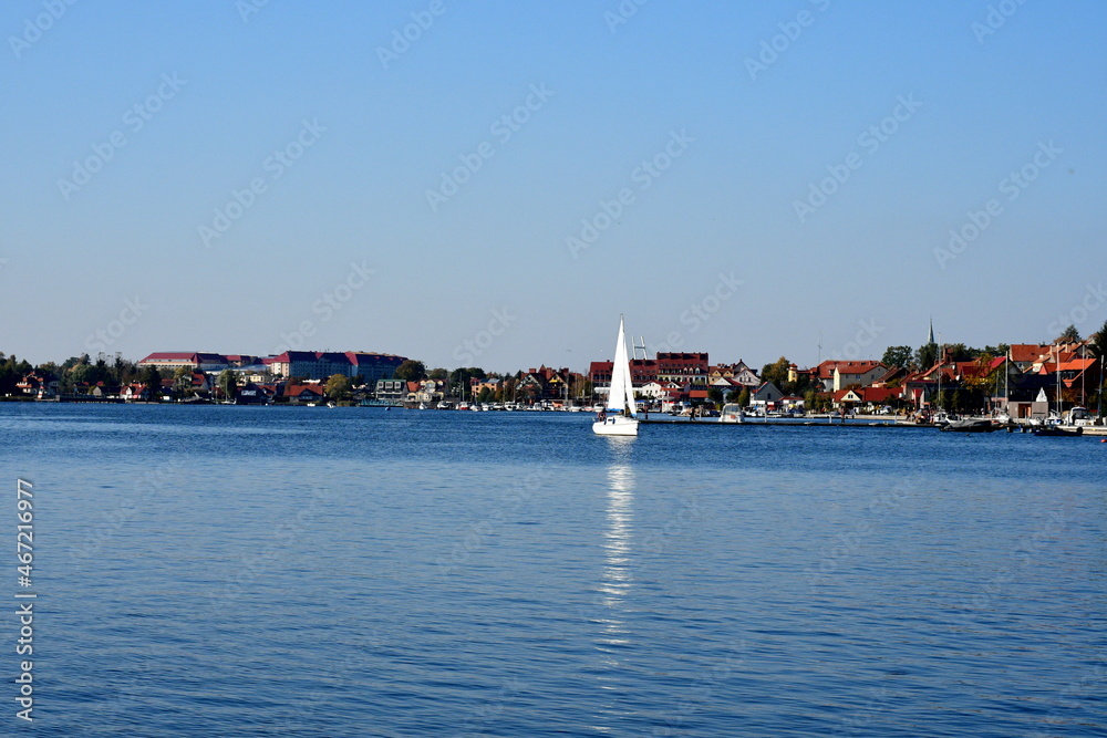 A view of a shallow yet vast river or lake covered from all sides with dense forest or moor with some ships and other vessels seen sailing through it on a cloudless summer day in Poland