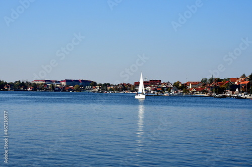 A view of a shallow yet vast river or lake covered from all sides with dense forest or moor with some ships and other vessels seen sailing through it on a cloudless summer day in Poland © Rafal