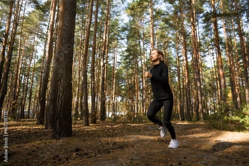 Young athletic woman jogging in forest in sunny morning. Healthy lifestyle concept.