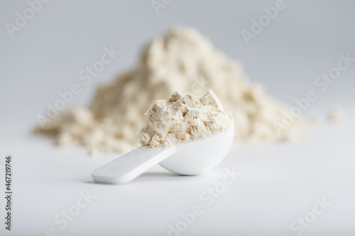 A pile of protein powder with a measuring spoon on a white background.