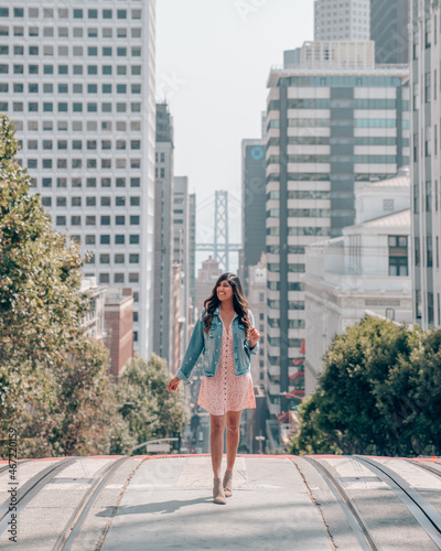 Woman in pink dress and denim jacket standing on the road near building photo