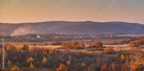 Panorama of the autumn landscape in the countryside in the evening. Young forest gives way to rural houses that end at the foot of the mountain