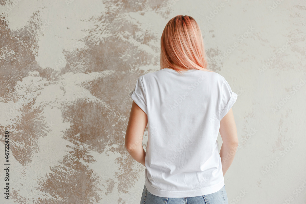 Young girl wearing blank white t-shirt. Back view. Concrete wall background