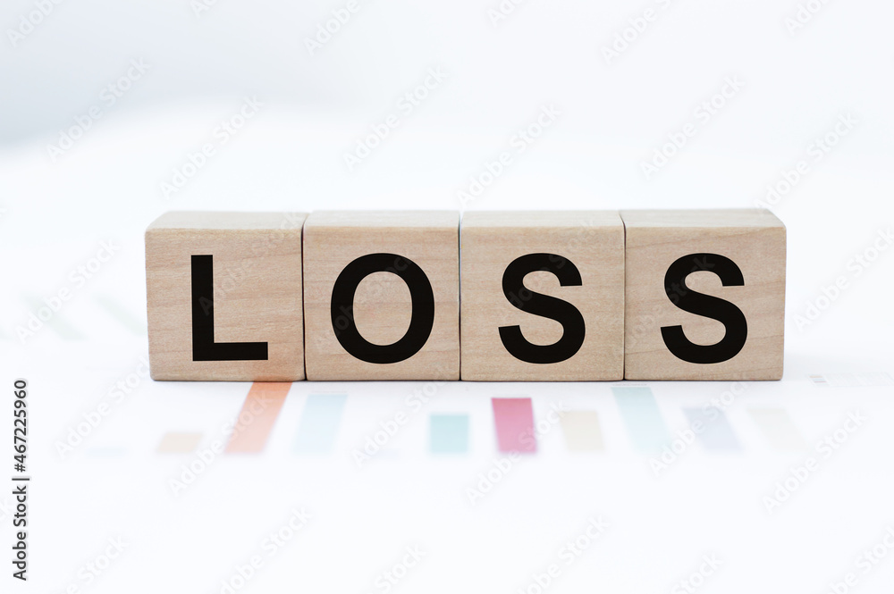 Wooden cubes with the text LOSS on the background of charts on the table Wooden cubes with the text LOSS on the background of charts on the table