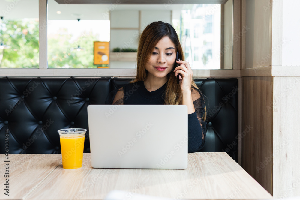 Businesswoman sitting at table in coffee shop and talking on mobile phone while working with laptop. Entrepreneur working outside office Businesswoman sitting at table in coffee shop and talking on mobile phone while working with laptop. Entrepreneur working outside office