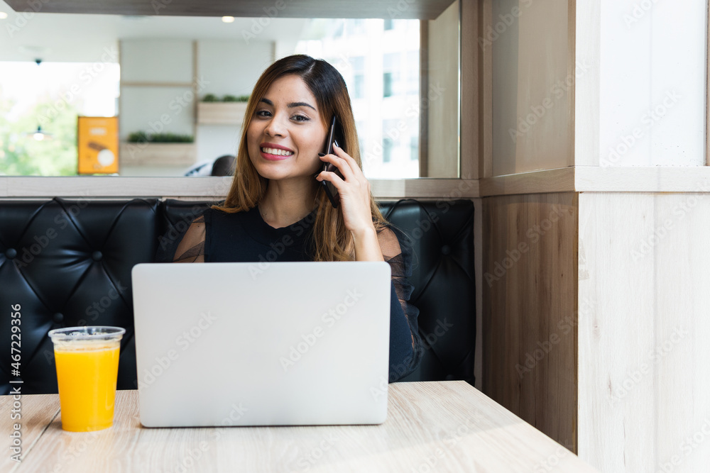 Portrait of smiling businesswoman looking at camera while talking on mobile phone and working with laptop. Business concept Portrait of smiling businesswoman looking at camera while talking on mobile phone and working with laptop. Business concept