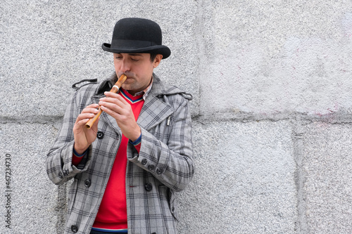 A man plays a musical instrument sopilka on the street against the background of the wall photo