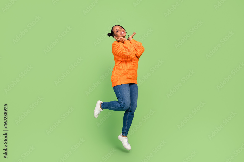 Full size photo of funky young brunette lady jump wear sweater jeans shoes isolated on green background Full size photo of funky young brunette lady jump wear sweater jeans shoes isolated on green background