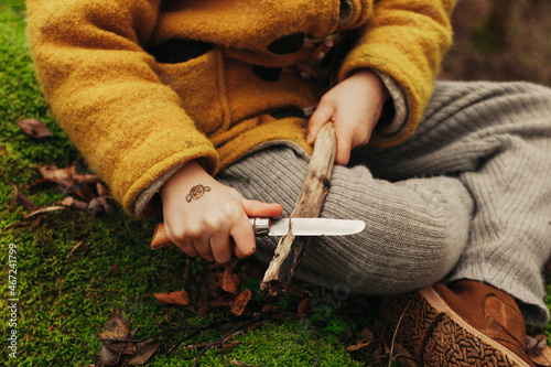 Hands of a Child Cutting Wooden Stick With a Knife photo
